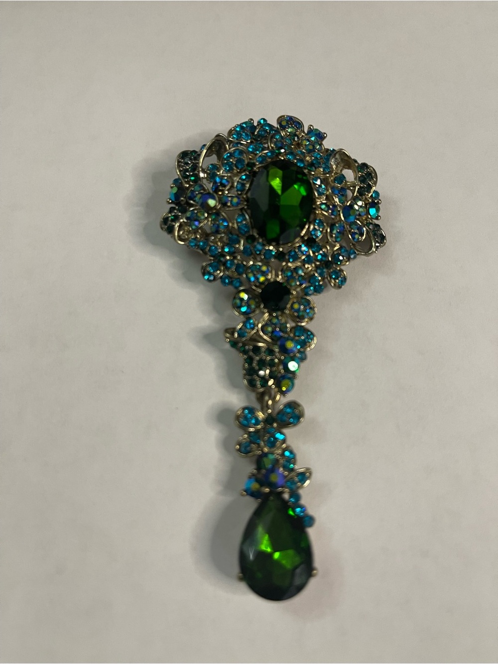 gold-tone teardrop pin featuring a central green crystal surrounded